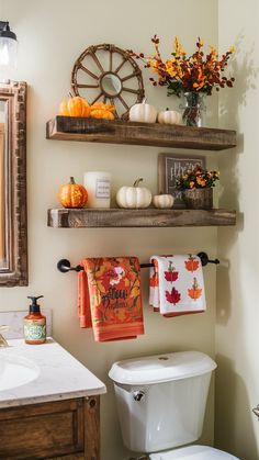 the bathroom is decorated with fall decor and pumpkins on the shelf above the toilet