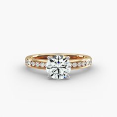 a gold engagement ring with diamonds on the band and a round cut diamond in the center