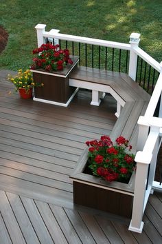 two planters with red flowers are sitting on a wooden deck next to a white railing