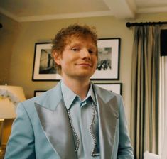 a man in a blue suit and tie standing next to a window with pictures on the wall behind him