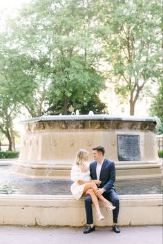 a man and woman sitting on a bench in front of a fountain