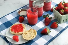 strawberry jam and bread on a blue checkered tablecloth with strawberries in the background