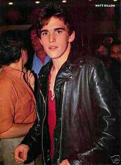 a young man in a leather jacket and red shirt standing next to a group of people