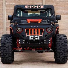 the front end of a black jeep with orange accents and large tires, parked in front of a garage door