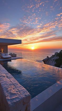 an outdoor swimming pool with the sun setting over the ocean in the backgroud