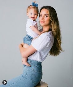 a woman sitting on top of a wooden stool holding a small child in her arms