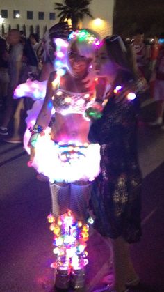 two women are standing on a scooter with lights all over it's body