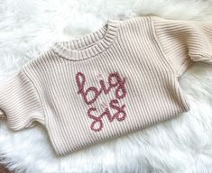 a sweater with the word big sister written on it sitting on a white furnishing