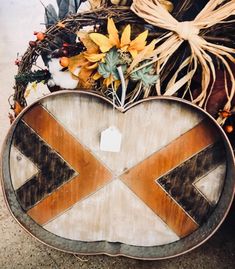 a wooden heart shaped sign sitting on top of a pile of leaves and other autumn decorations