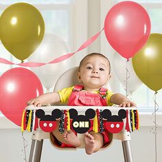 a baby is sitting in a high chair with balloons