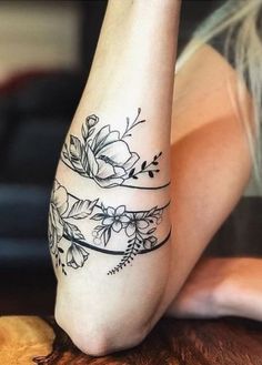 a woman's foot with flowers on it and a ribbon around the ankle tattoo