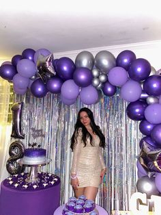 a woman standing in front of a table with purple and silver balloons on it's wall