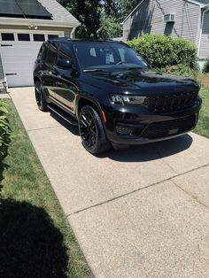 a black jeep parked in front of a house on a driveway with grass and bushes