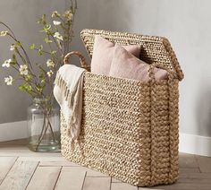 a basket sitting on the floor next to a vase with flowers in it and a throw pillow