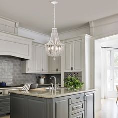 a chandelier hanging from the ceiling in a kitchen with white cabinets and gray countertops