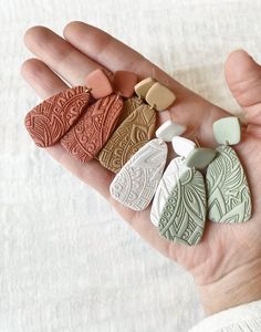 a person's hand holding five different colored clay pieces in their palm, with white linen behind them