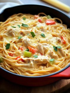 pasta with chicken and vegetables in a red skillet on a wooden table next to a yellow fork