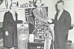 two men and a woman standing next to each other in front of a vending machine