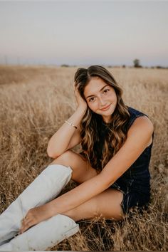 a woman sitting in the middle of a field with her hand on her head and looking at the camera