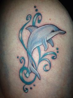 a dolphin tattoo on the back of a woman's shoulder, with swirls and waves