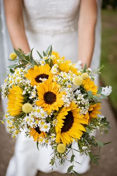 a bride holding a bouquet of sunflowers and daisies