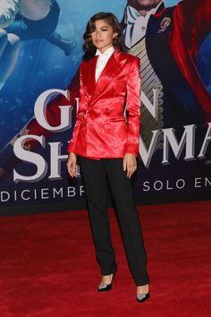 a woman in a red jacket and black pants on the red carpet at an event