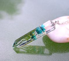 a necklace with flowers on it sitting on top of a rock next to a leaf