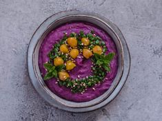 a bowl filled with purple hummus and garnished with green leafy garnish