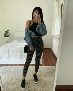 a woman taking a selfie in front of a mirror wearing striped pants and denim jacket