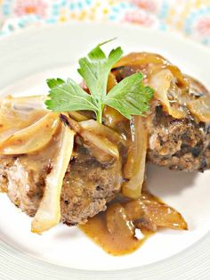 a white plate topped with meat covered in gravy and onions on top of a wooden cutting board