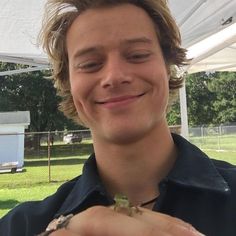 a smiling young man holding a small lizard in his right hand under a white tent