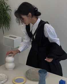 a woman standing over a vase on top of a table