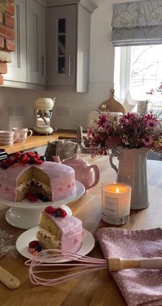 a table topped with cakes and candles on top of wooden counter tops next to a vase filled with flowers