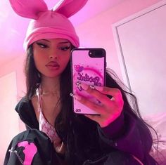 a woman taking a selfie with her cell phone wearing a pink bunny ears hat