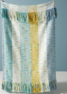 a blanket with fringes hanging on a clothes line in front of a blue wall