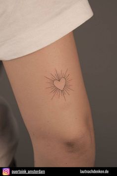 a small sun tattoo on the left side of the leg, with a heart in the middle