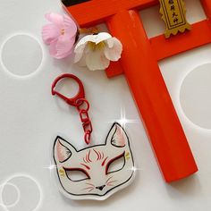 a keychain with a cat face on it next to a flower and an orange frame