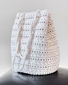 a white crocheted bag sitting on top of a black table next to a wall