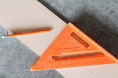 an orange plastic triangle with a pencil on the side and a ruler in front of it