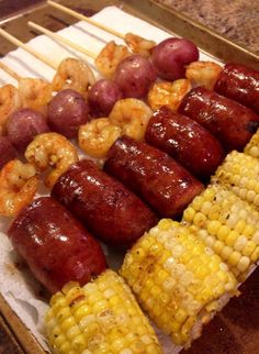 corn on the cob, shrimp and potatoes are being grilled with skewers