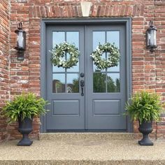 two large planters with wreaths on them are in front of a gray door