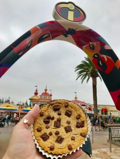 a person holding a chocolate chip cookie in front of an arch at a theme park