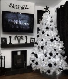 a white christmas tree with black ornaments in front of a large screen tv mounted on the wall