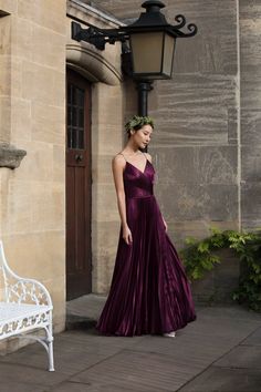 a woman in a long purple dress standing next to a white bench and lamp post