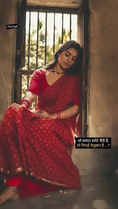 a woman sitting on the ground wearing a red sari and holding her hands in her lap