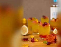 three glasses filled with drinks sitting on top of a wooden table next to lemon slices and candies