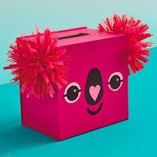 a pink box with red pom - poms on the front and sides, sitting on a blue surface