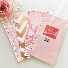 three notebooks with pink flowers and gold foil on them, next to a flower