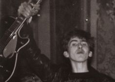 black and white photograph of a man holding a guitar in his right hand, looking up at the sky