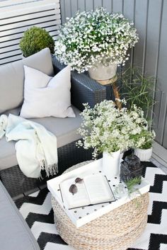 an outdoor patio with white flowers and plants in baskets on the floor, next to a wicker basket filled with books